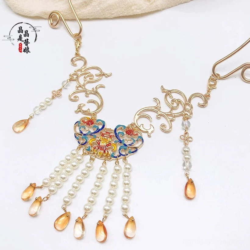 Dunhuang-inspired Chinese necklace with gold floral enamel pendant, freshwater pearl tassels, and amber teardrop charms on beige linen