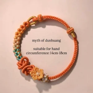 Dunhuang inspired handwoven Chinese knot bracelet in warm orange cord with gradient braided details, traditional knot ornaments, and gold-tone floral gem charm on a light pink background