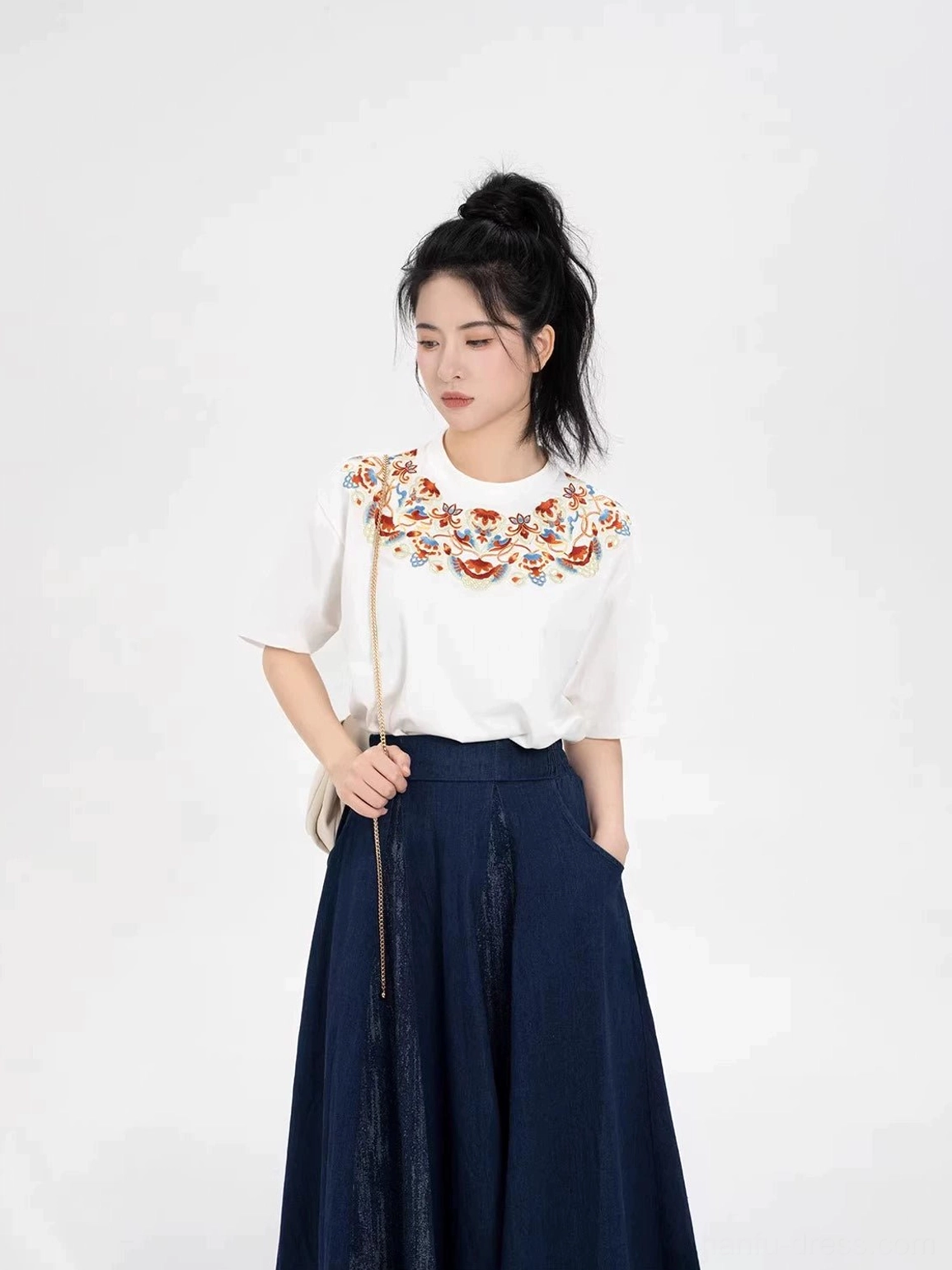 Dunhuang-inspired embroidered white T-shirt and long navy skirt outfit styled with a beige shoulder bag