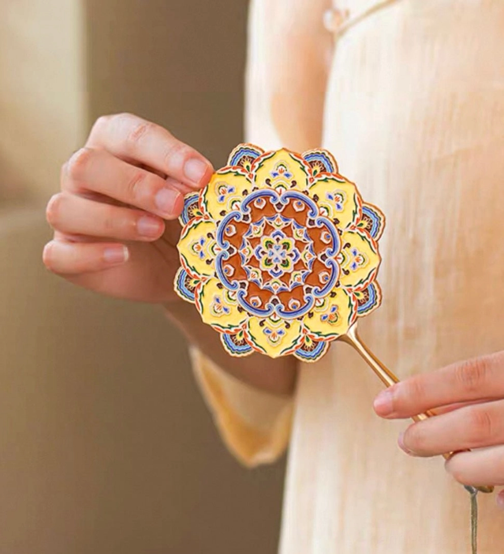 Full side view of a Dunhuang-inspired Chinese hand mirror held with traditional Chinese clothing, showing the ornate lotus caisson pattern, gold-tone handle, and decorative hanging tassel