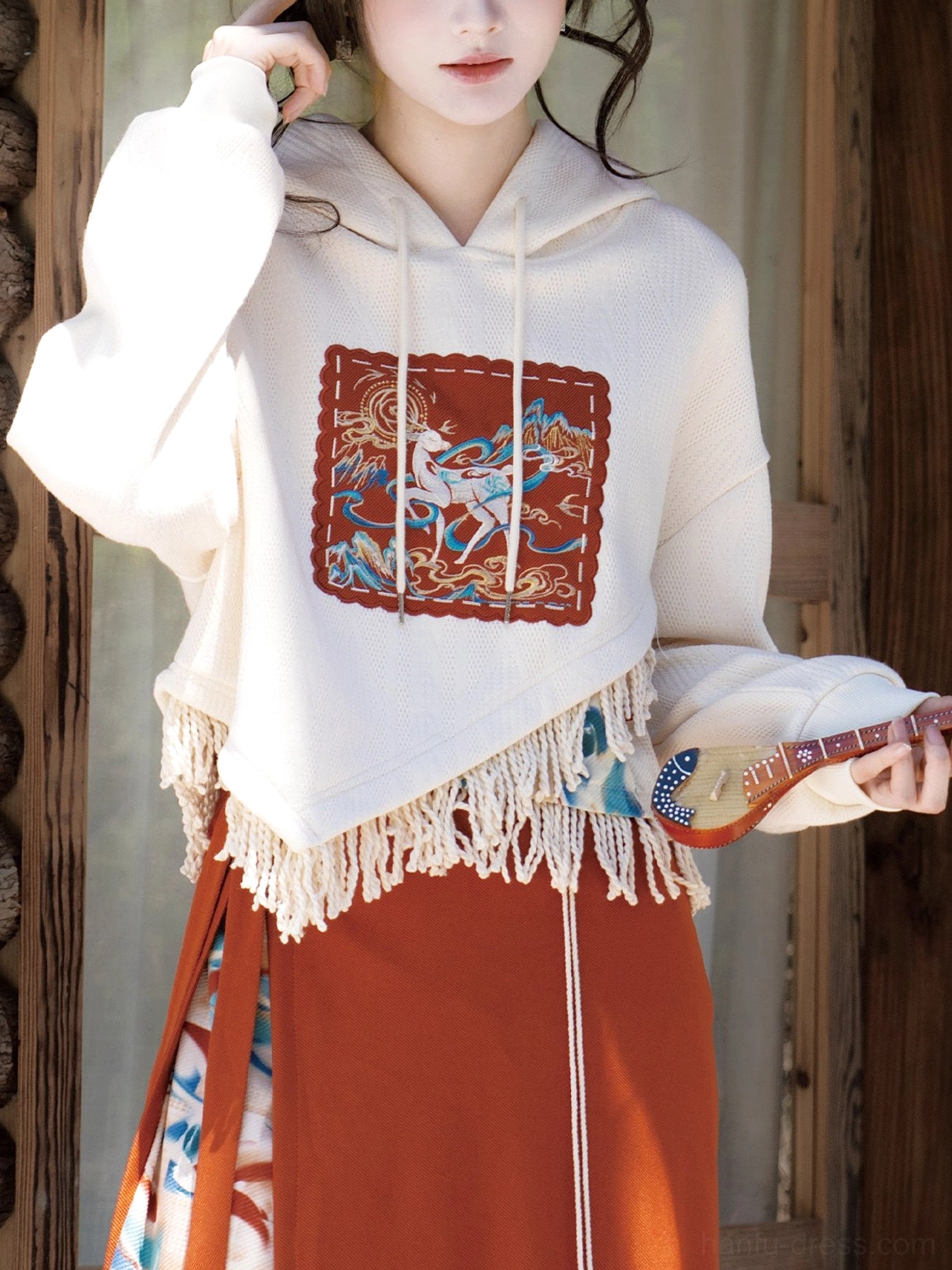 Close-up of the ivory Dunhuang Singing Deer cropped hooded sweater with embroidered traditional Chinese art patch and asymmetric tassel fringe