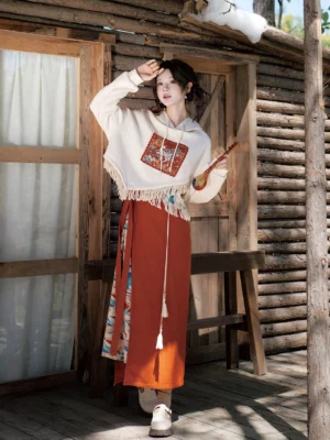 Dunhuang Singing Deer modern Hanfu two-piece outfit with ivory tassel hooded sweater and terracotta wrap skirt shown in a full-body three-quarter view