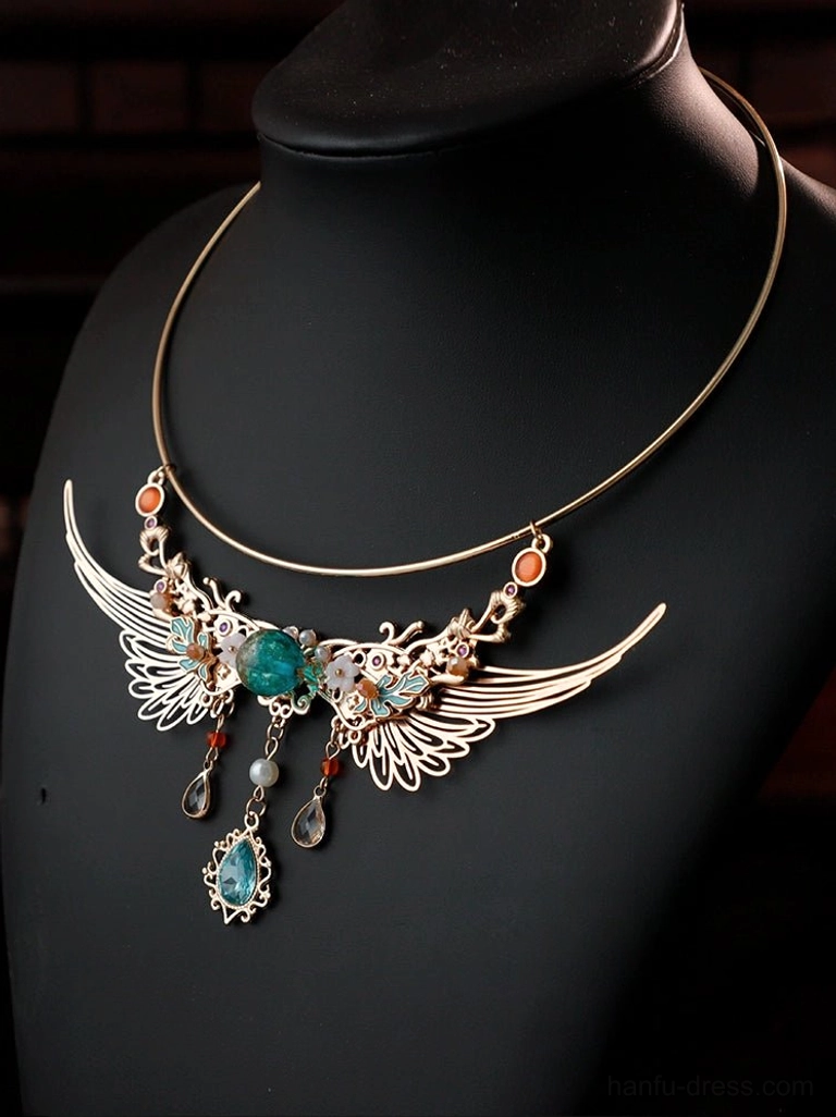 Three-quarter view of a Dunhuang-style winged Chinese collar necklace on a black mannequin bust, showing the gold-tone frame, carved wing details, green focal gem, beads, and layered hanging pendants