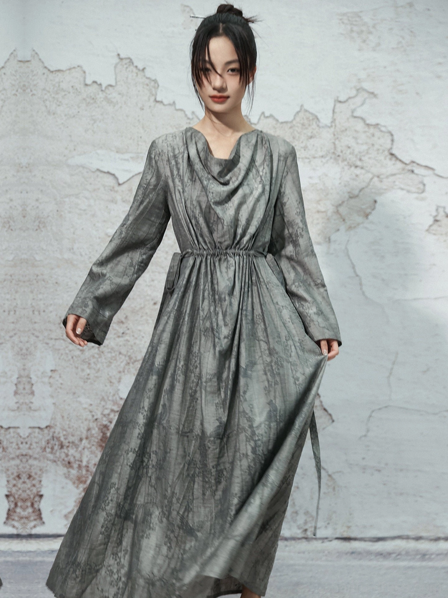 Three-quarter view of grey marbled Chinese-style maxi dress with draped cowl neck, long sleeves, flowing skirt and hanging waist sash