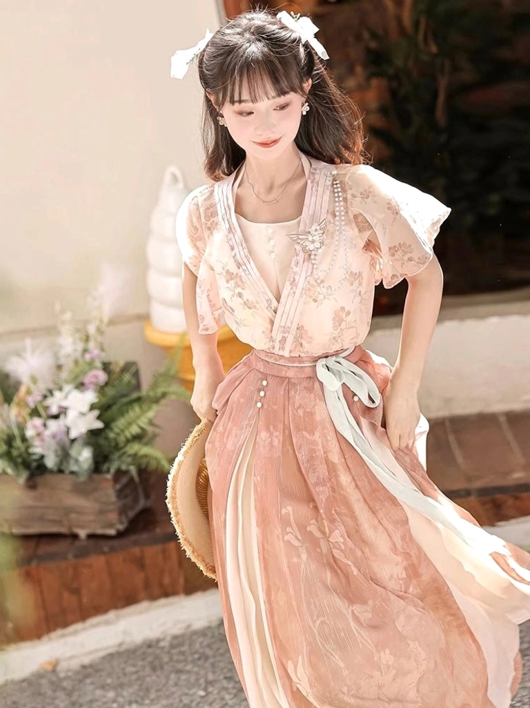 Front three quarter view of a dusty pink floral modern Wei-Jin style Hanfu set with chiffon coat ruffled sleeves cross V-neck camisole and flowing high waisted skirt