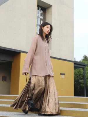 Side walking view of a modern autumn Hanfu outfit with dusty pink round collar top, wide bishop sleeves, bronze pleated mamianqun horse face skirt, and black crossbody bag