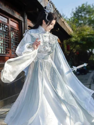Eastern Emperor xianxia hanfu for men in a white and pale blue-gray Northern and Southern Dynasties-inspired costume, featuring an embroidered round-collar robe, flowing wide sleeves, trailing cloak, layered inner garments, silver hair crown, and decorative sword in a traditional Chinese courtyard