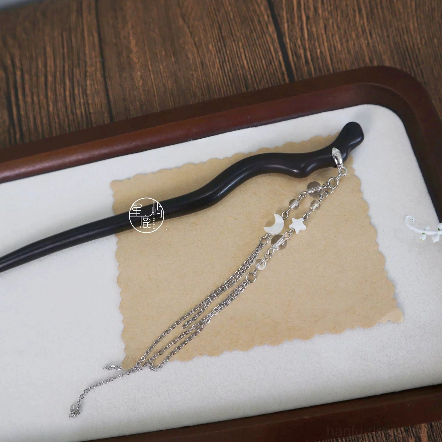 Dark curved Chinese hair stick and celestial moon star chain tassel displayed on a wooden tray flat lay