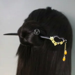 Elegant Chinese hair stick with dark wooden shaft golden floral decoration and amber tassel securing a neat low bun for Hanfu or qipao styling
