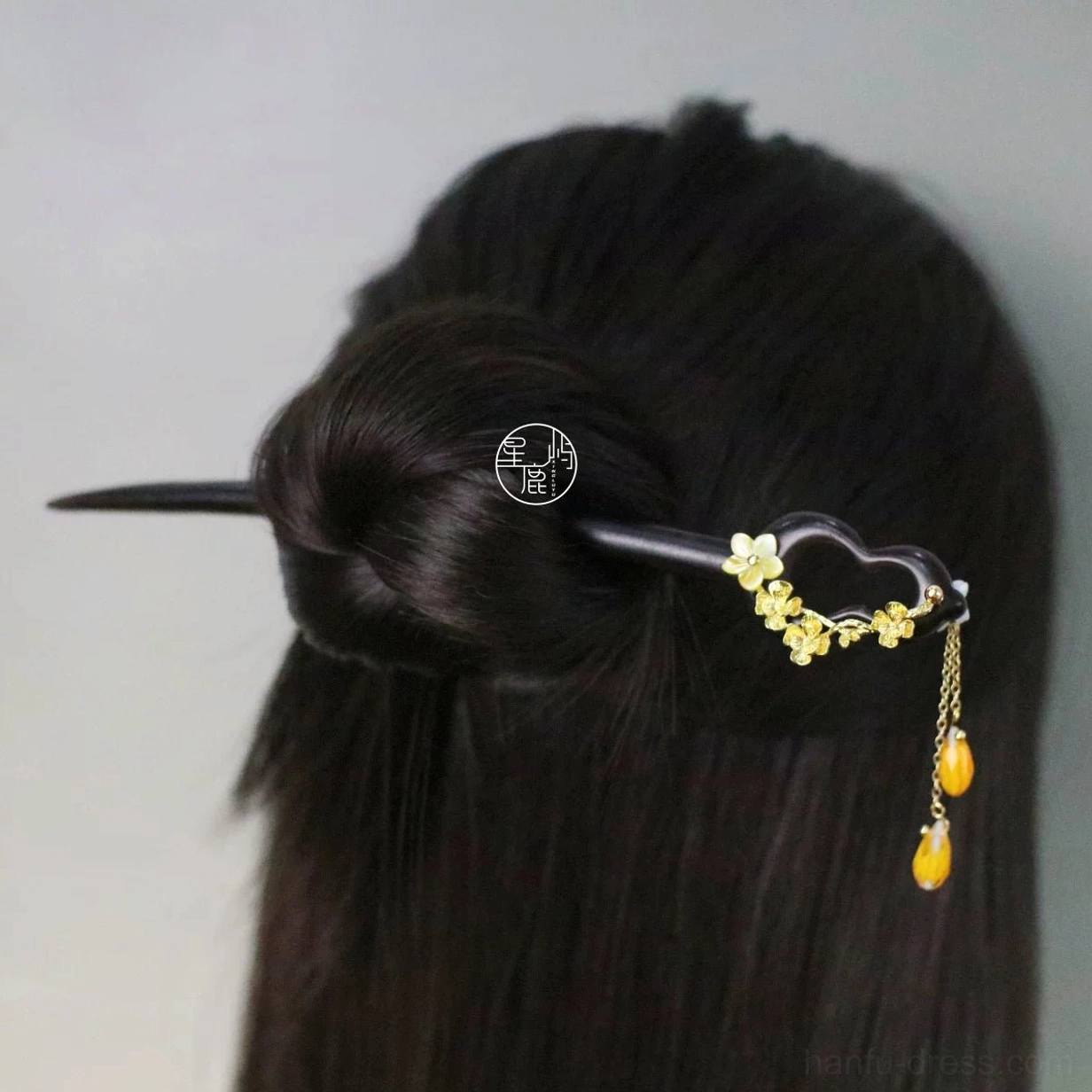 Elegant Chinese hair stick with dark wooden shaft golden floral decoration and amber tassel securing a neat low bun for Hanfu or qipao styling