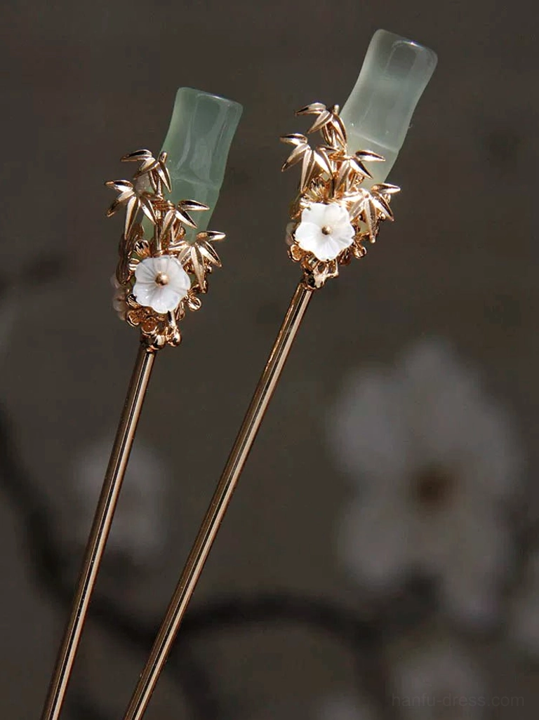 Pair of elegant jade green bamboo Chinese hairpins with gold tone leaf details against dark floral background