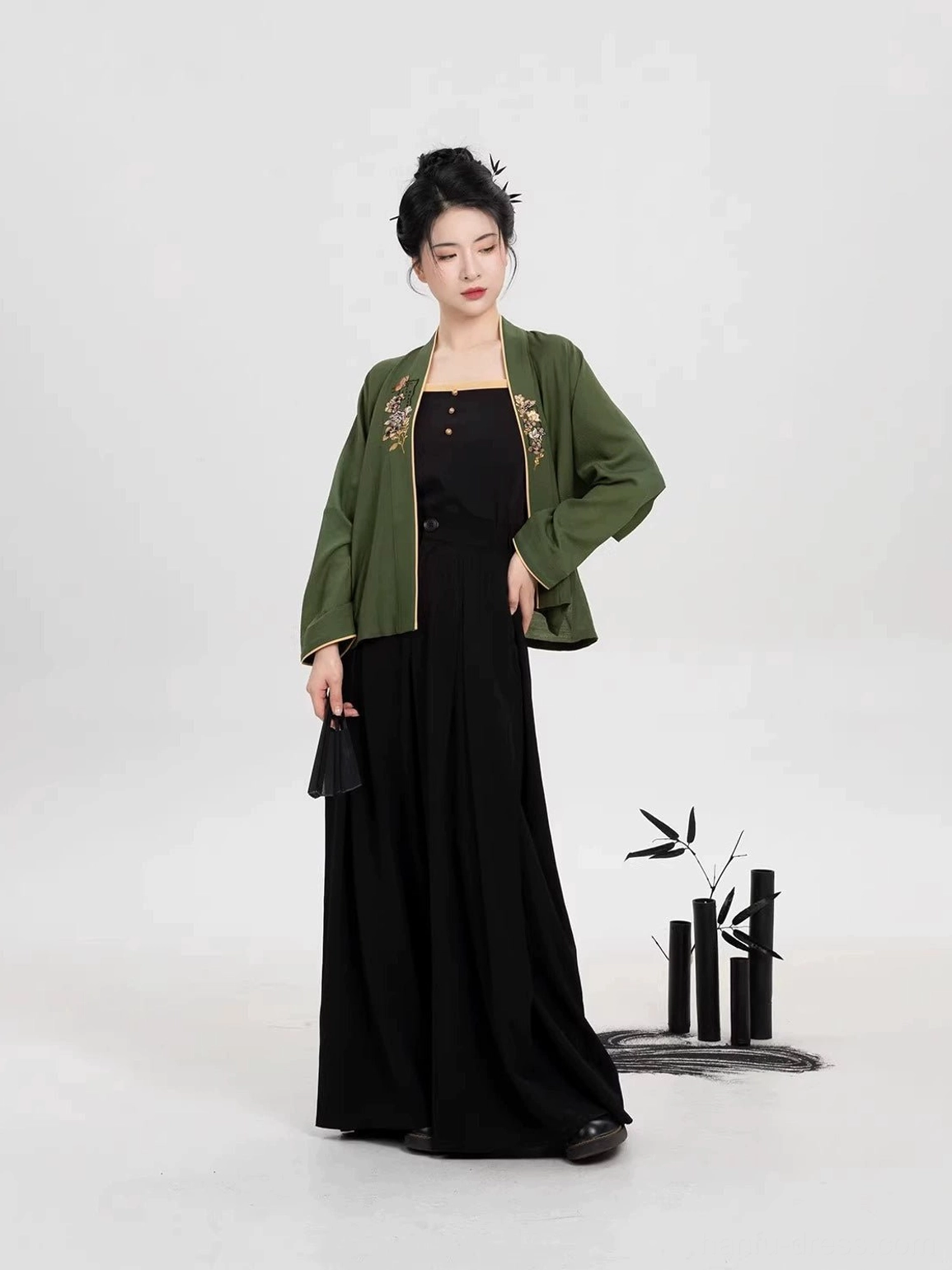 Elegant three piece modern Hanfu clothing set with embroidered green top and coordinated black wide leg trousers side standing view