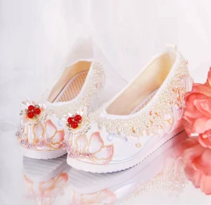 White embroidered Chinese Hanfu shoes for women with pink and gold lotus embroidery, pearl trim, red bead tassel ornament, and raised rubber sole