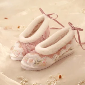 Women's pink and white embroidered traditional Chinese Hanfu shoes with floral toe embroidery, fluffy fleece trim, ribbon heel bow, lace detailing, and flexible rubber soles displayed on beige fabric with pearl and flower decorations