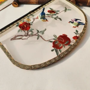 Close-up front view of a decorative knife-shaped Chinese hand fan showing colorful embroidered songbirds, red flowers, green branches, pomegranates, translucent fabric, and geometric brocade-style trim