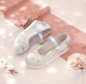 Traditional embroidered Chinese Hanfu cloth shoes for women in an overhead flat lay, featuring an off-white canvas upper, light blue and yellow floral embroidery, blue buckle straps, breathable mesh insoles, and low rubber wedge heels