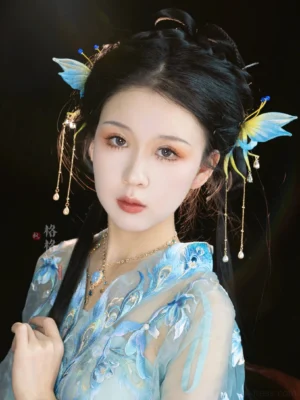 Model wearing emerald butterfly Hanfu hair pins with blue bead accents and dangling tassels styled with a light blue embroidered traditional Chinese Hanfu outfit