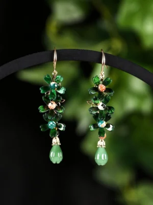 Emerald green floral Chinese drop earrings with gold-tone hooks and jade-green teardrop pendants displayed on a black jewelry rod