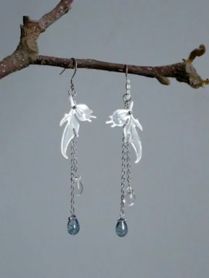 Fairy immortal goldfish dangle earrings with iridescent white fish pendants, silver chains, clear teardrop beads, and deep blue charms displayed on a dry tree branch