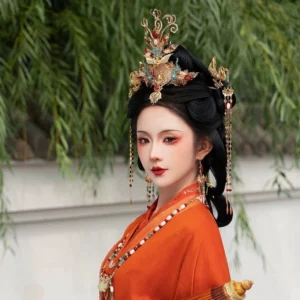 Elegant hanfu formal hair jewelry set shown on a woman wearing an orange Chinese traditional dress, with an ornate phoenix headpiece, matching hair ornaments, layered beads, and Tang-inspired makeup