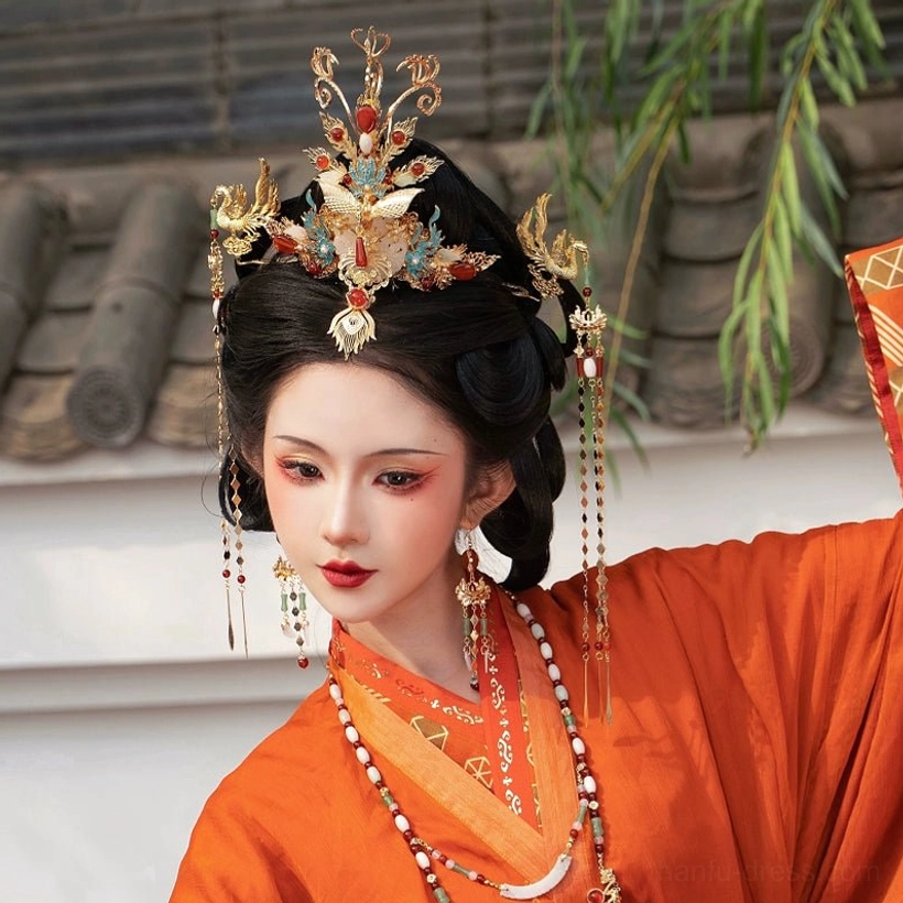 Traditional Chinese hanfu hair accessories set styled on a woman in a burnt orange robe, featuring a gilded phoenix crown, beaded hanging tassels, matching drop earrings, and layered traditional jewelry beside an ancient grey brick wall