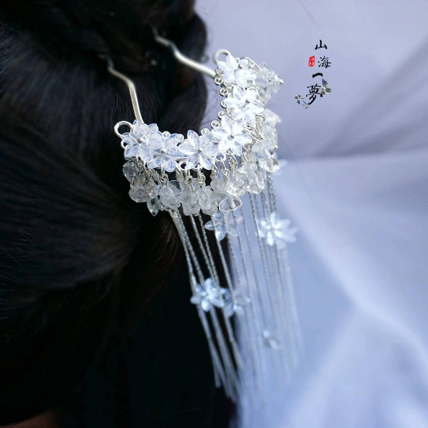 Falling Snow silver-tone Chinese hair pin worn in a traditional dark hair bun, showing sparkling crystal flowers, white floral charms, and flowing double tassels