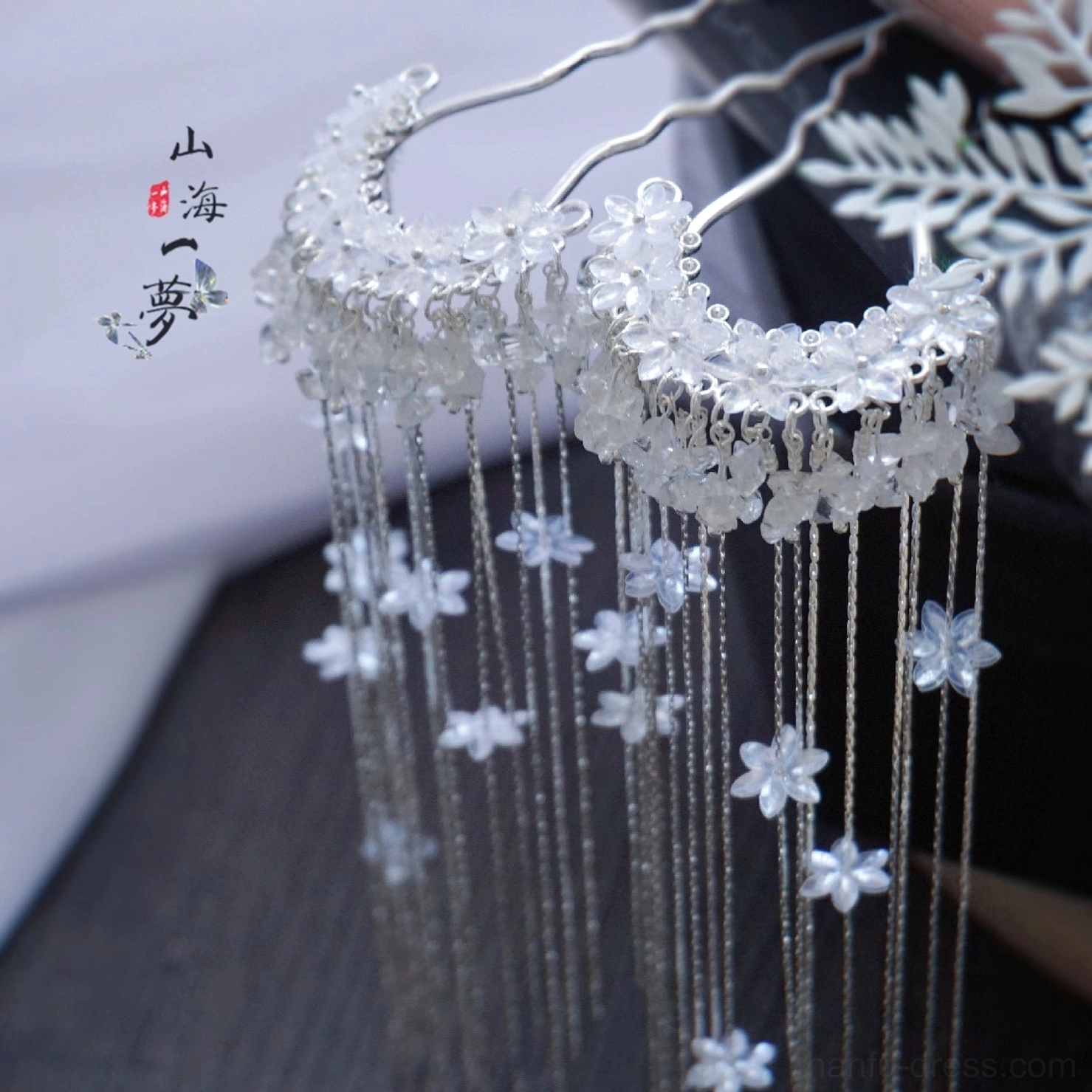 Falling Snow Chinese hanfu hair pin displayed on a dark wooden table with crystal flower ornaments, silver-tone metalwork, white floral pendants, and elegant double tassels