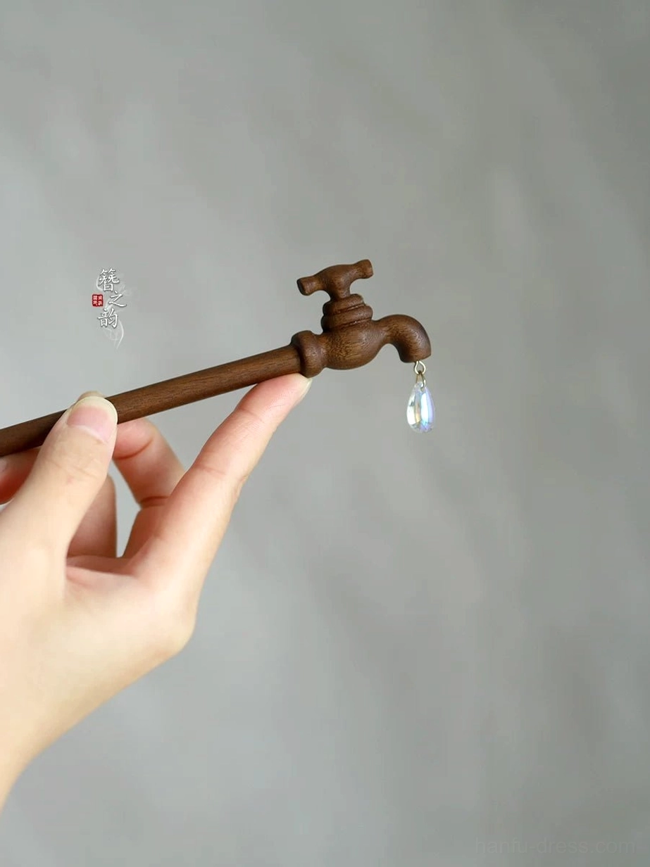 Close-up of faucet shaped wooden Chinese hair stick showing carved tap handle spout wood grain and iridescent pendant