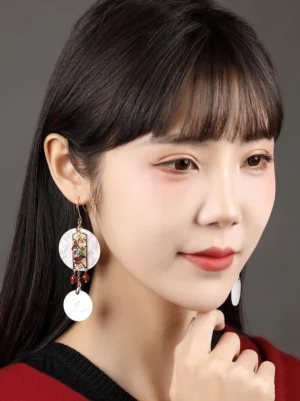 Female model wearing elegant Chinese shell drop earrings with red bead tassels styled with a red and black outfit