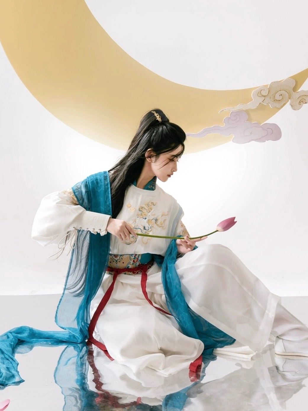 Profile view of female warrior xianxia hanfu costume in white teal blue and red with lotus flower prop