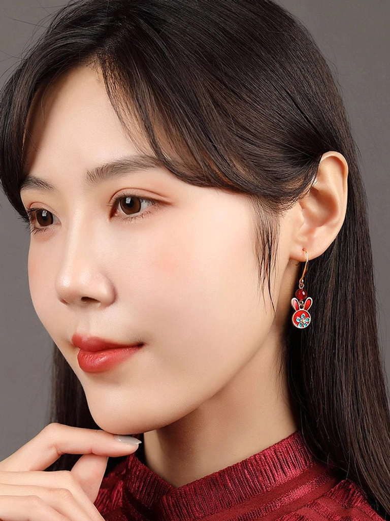 Model in a dark red cheongsam wearing festive rabbit earrings with red enamel charm and blue floral Chinese-inspired details