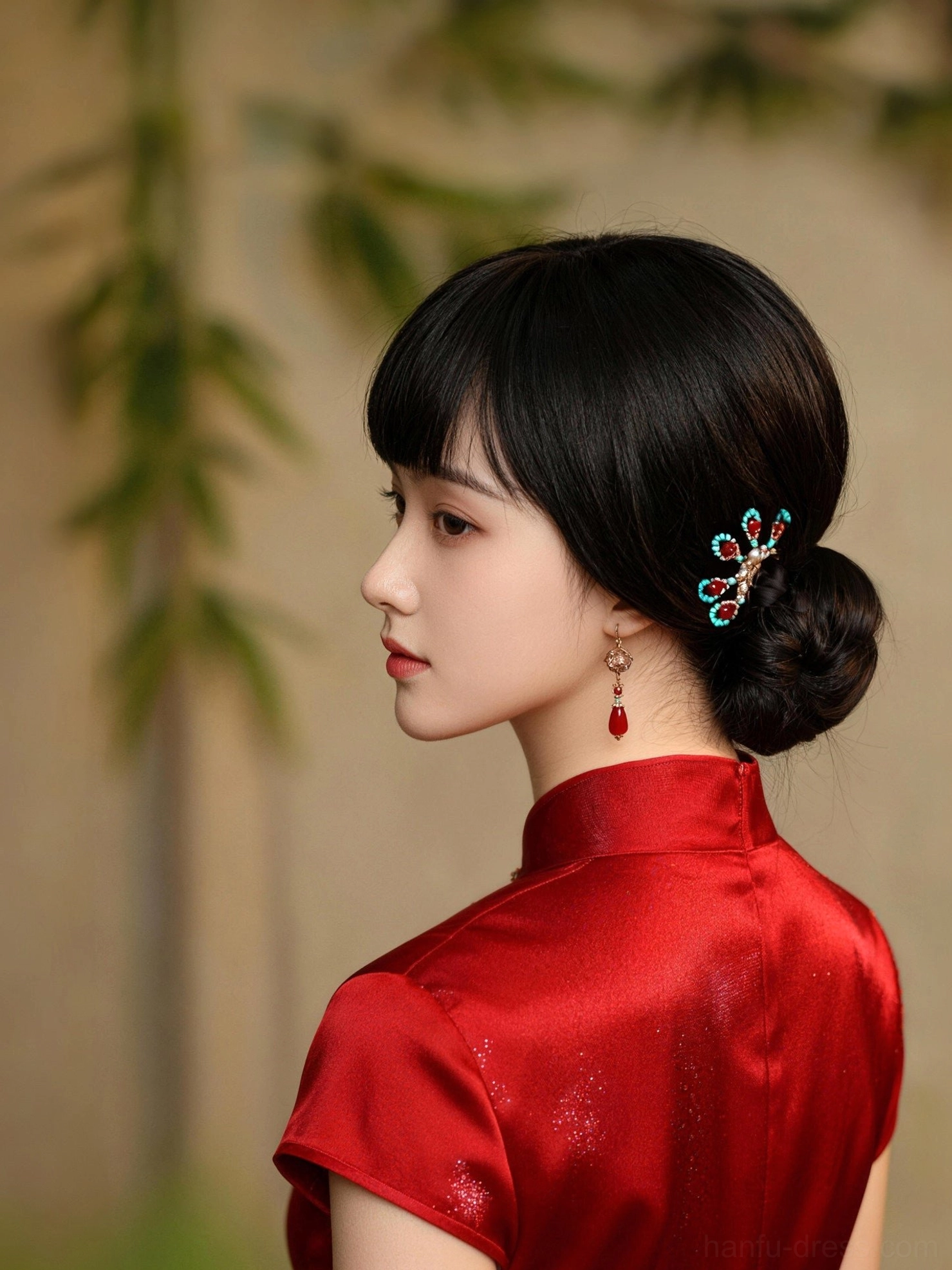 Side portrait of model styling red agate Chinese earrings with red satin Qipao and classic low bun