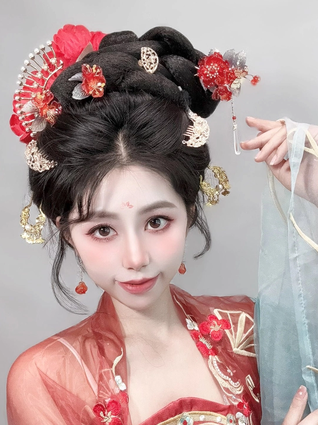 Woman wearing festive red blossom Hanfu hairpins and side ornaments in a traditional Chinese coiled hairstyle with red Hanfu costume