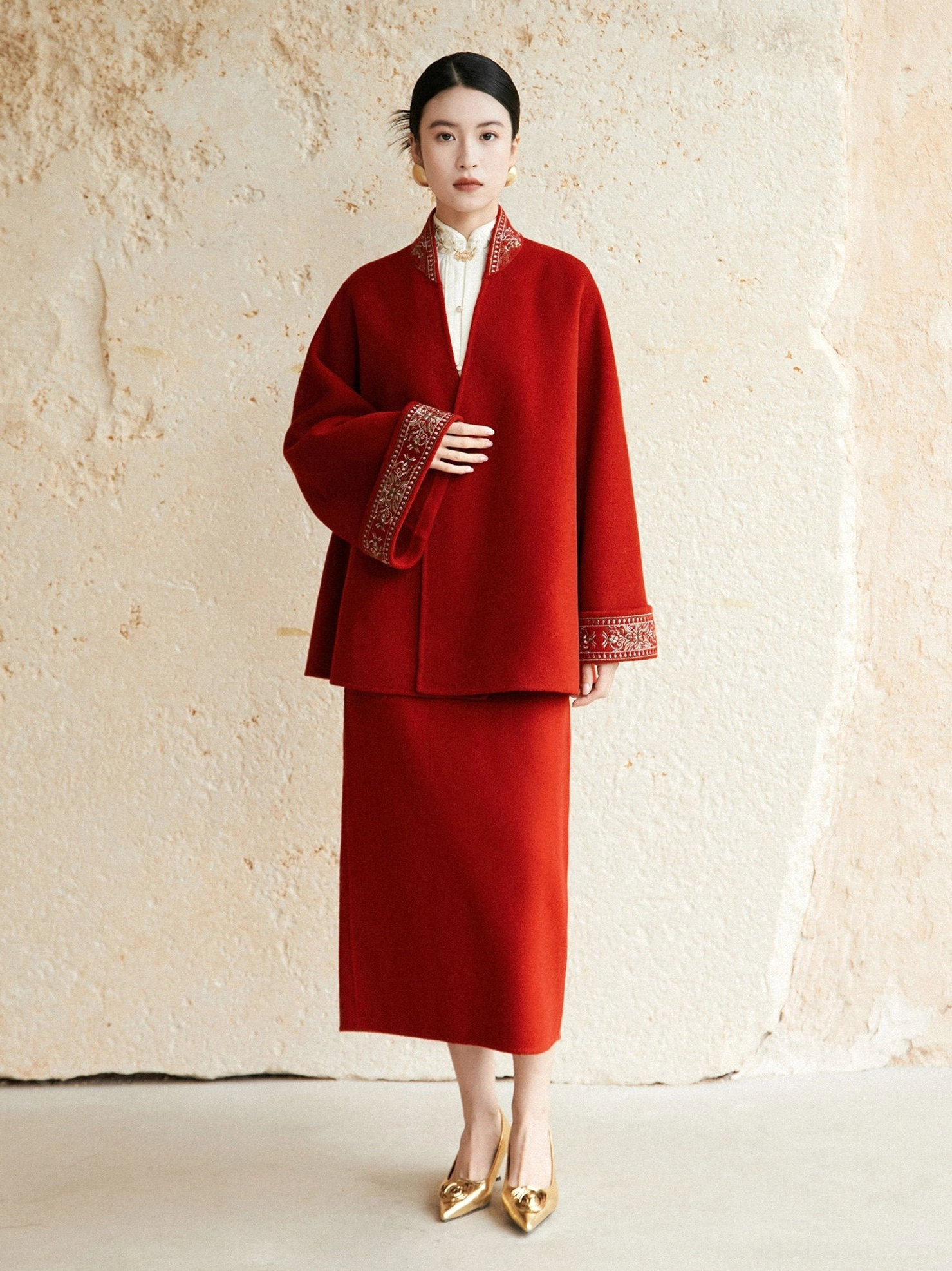 Three quarter view of festive red Hanfu inspired wool coat with embroidered sleeve cuffs and tailored midi skirt styling