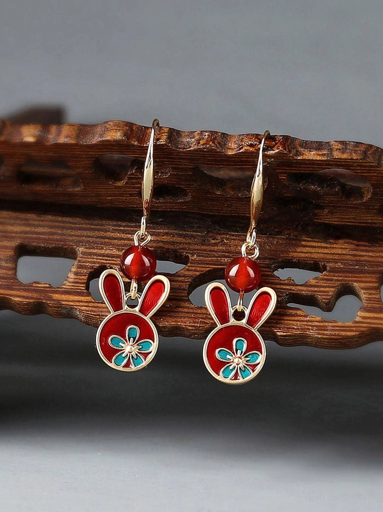 Festive red rabbit drop earrings displayed on a carved wooden shelf with gold ear wires, red beads, and blue floral enamel details
