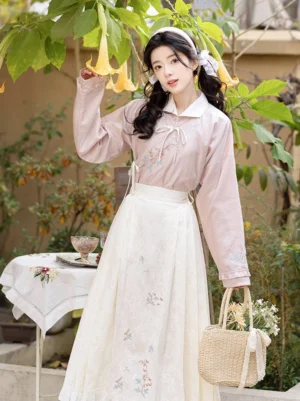 Fish and peony Ming-inspired hanfu set with dusty pink embroidered long sleeve top and ivory mamian skirt in a garden