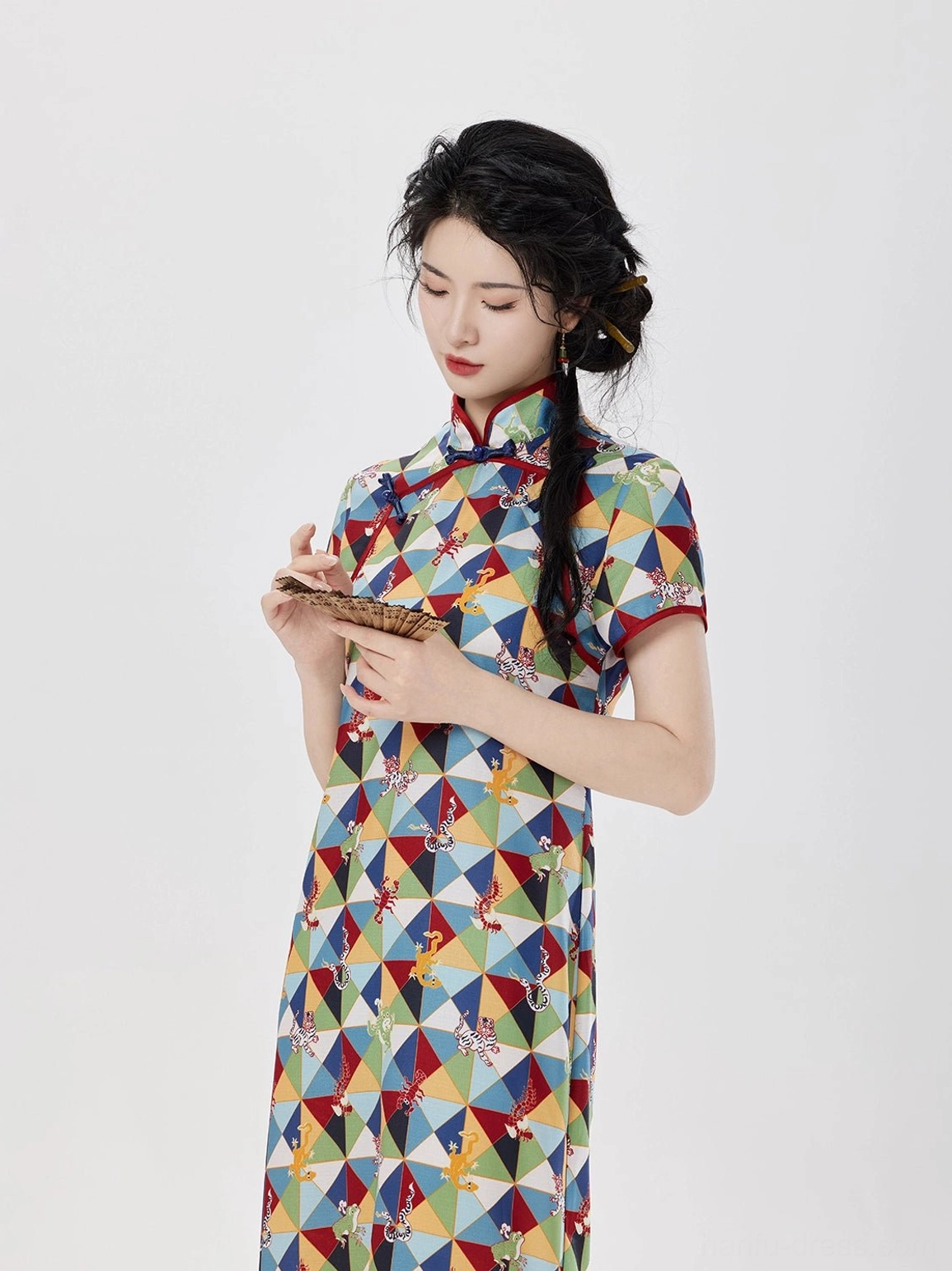 Close-up of Five Poisons modern Hanfu qipao showing colorful geometric print, red contrast stand collar, short sleeve trim, and folding fan styling