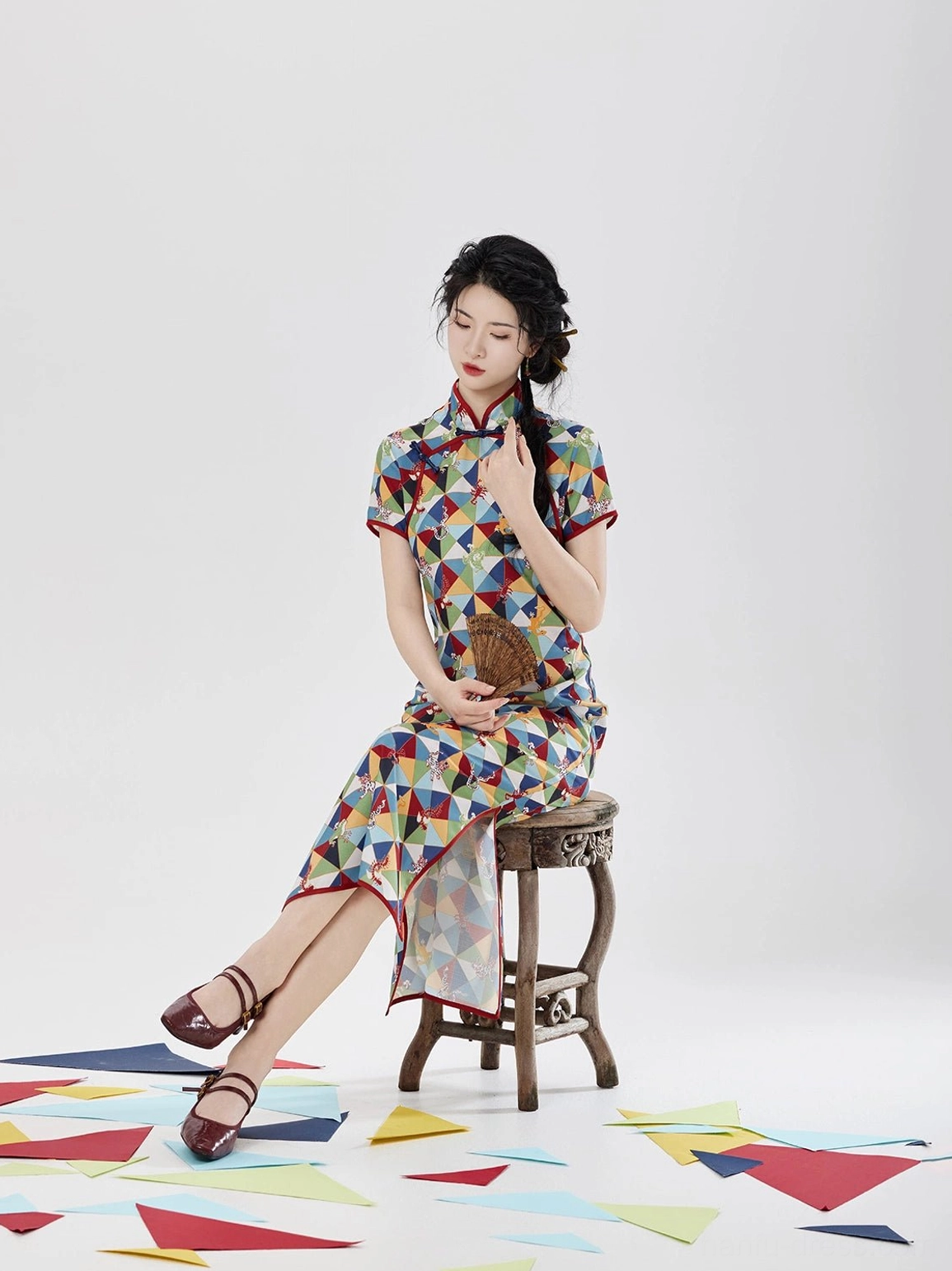 Three-quarter seated side view of Five Poisons qipao midi dress with fitted silhouette, short sleeves, red trim, and high side skirt slit