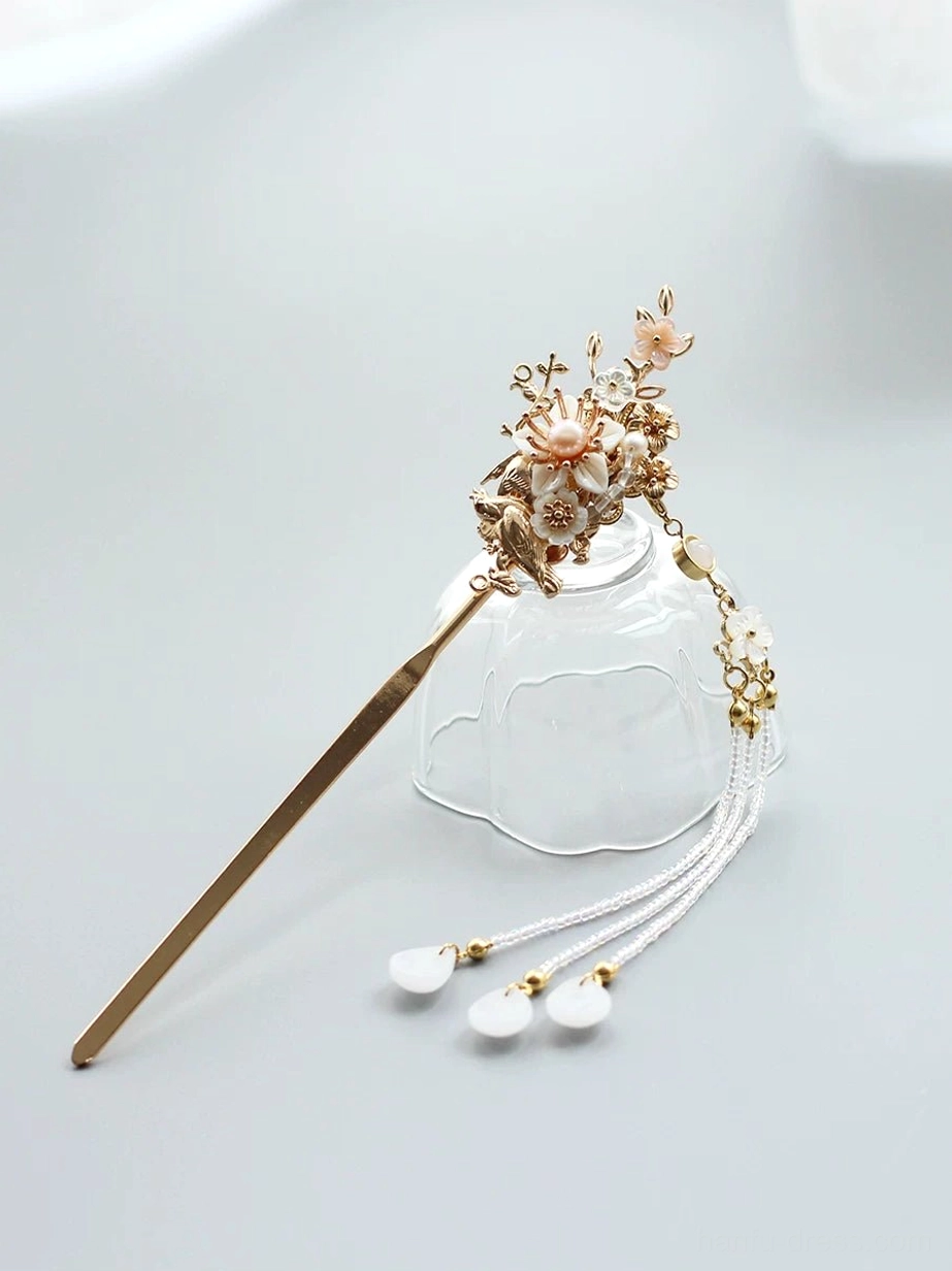 Floral bird Chinese hair stick with gold-tone ornament, pink flowers, white tassel, and drop pendants displayed on a clear glass teacup