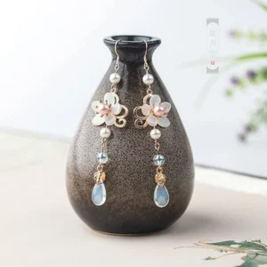 Floral Hanfu drop earrings with milky white and pink flowers pearl chains blue bead accents and opal teardrop charms displayed on a vintage Chinese ceramic vase