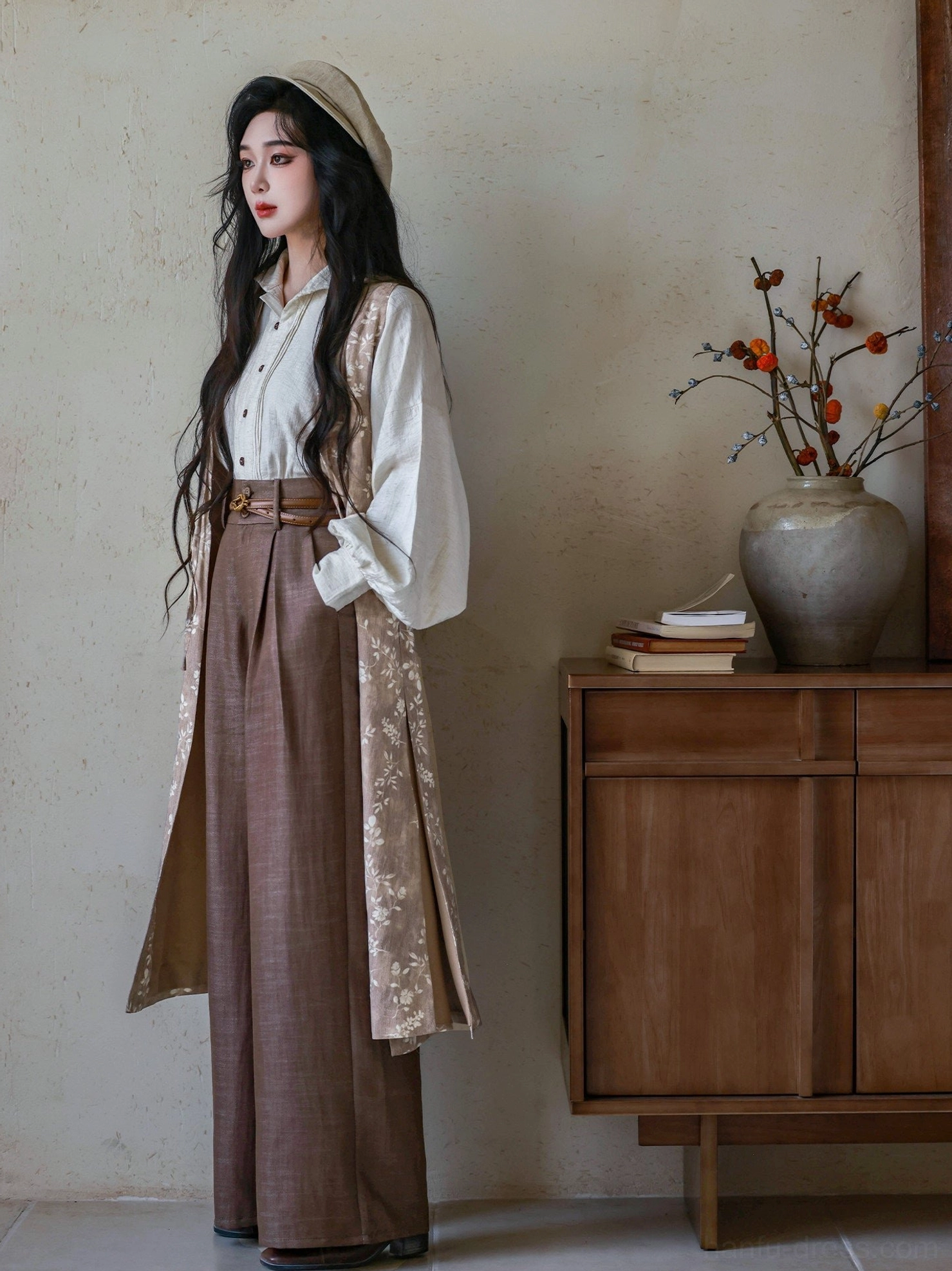 Side full-body view of a floral long hanfu robe layered over a light top and brown wide leg pants with a leather waist belt