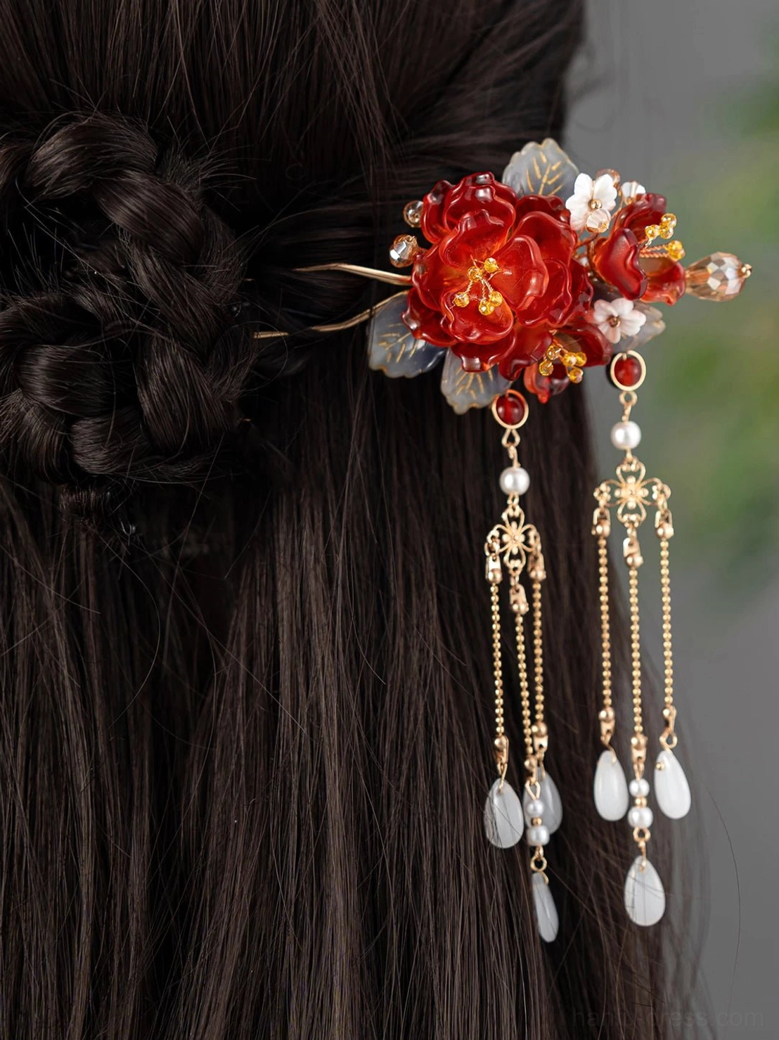 Woman wearing a floral tassel Chinese hair stick in a traditional braided updo with the elegant red peony ornament and hanging chains visible