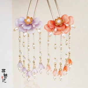 Lavender purple and warm orange floral tassel hair pins displayed on a light background with flower ornaments pearl-like centers golden accents beads and dangling bell pendants