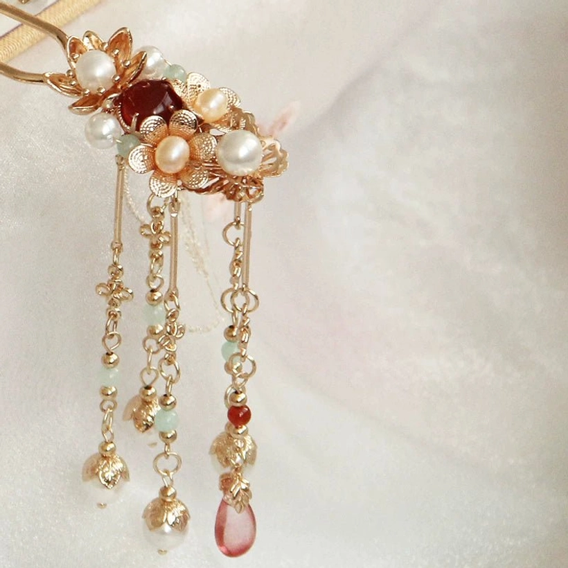 Close-up of Flower Festival Chinese hair stick showing intricate gold-tone floral filigree burgundy center gem faux pearls chain tassels and red teardrop pendant