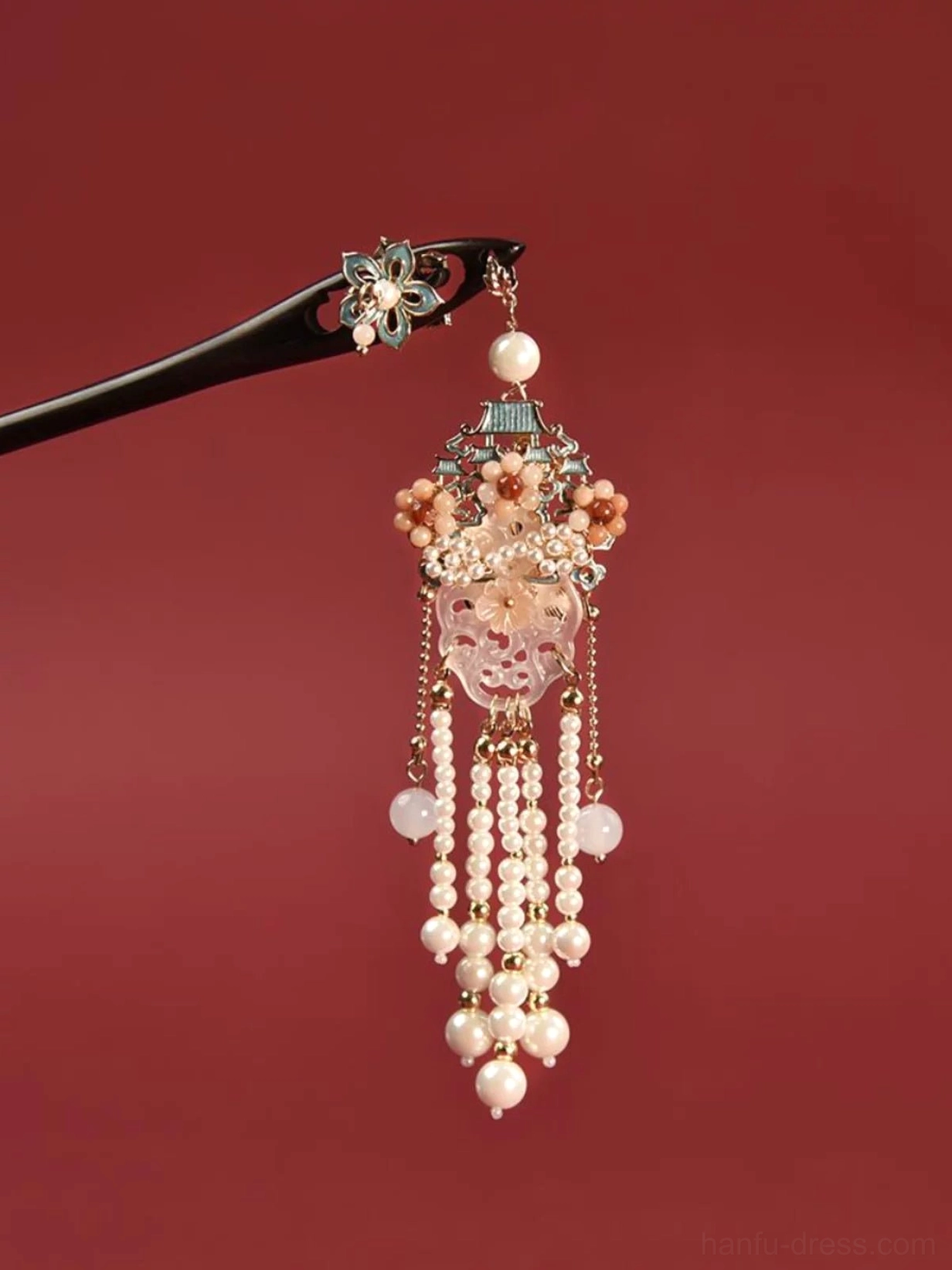 Flower-themed Chinese hair stick with delicate enamel flower, pink floral accents, carved jade-inspired pendant, and pearl tassel decoration shown against a dark red background