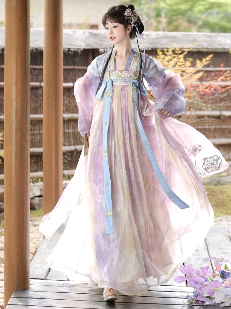 Front three quarter view of a woman wearing a flowing pastel gradient Tang Dynasty Hanfu dress with embroidered skirt hem in an autumn garden