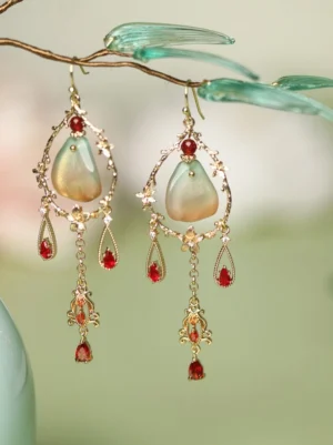 Three-quarter view of Dunhuang-style Hanfu drop earrings with ornate gold-tone metalwork, green gradient teardrop pendants, and red tassels