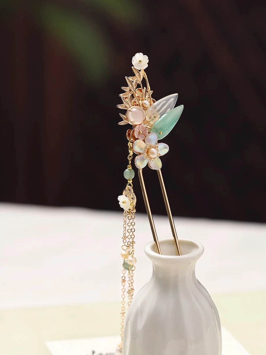 Traditional Chinese hair stick with gold-tone floral ornament, jade-green leaves, pink and white flowers, imitation pearl beads, and long double tassels displayed in a white ceramic vase