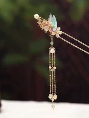 Close-up of a traditional Chinese tassel hairpin showing layered beaded chains, imitation pearl pendants, green leaf details, and gold-tone floral hair ornament against a dark green background