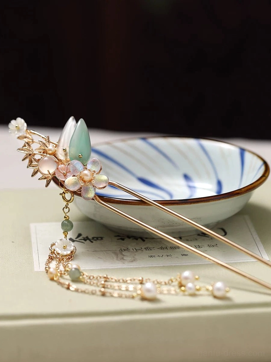 Chinese hair stick with floral leaf ornament and complete pearl beaded tassel arranged on a book beside a blue and white porcelain bowl